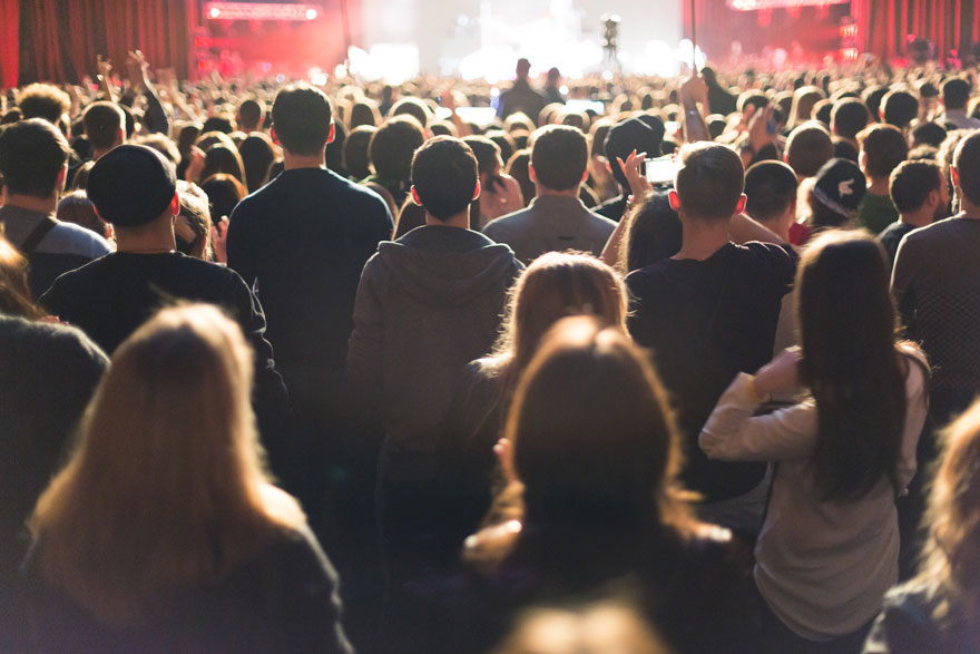 standing crowd of people watching an entertainer on a brightly lit stage